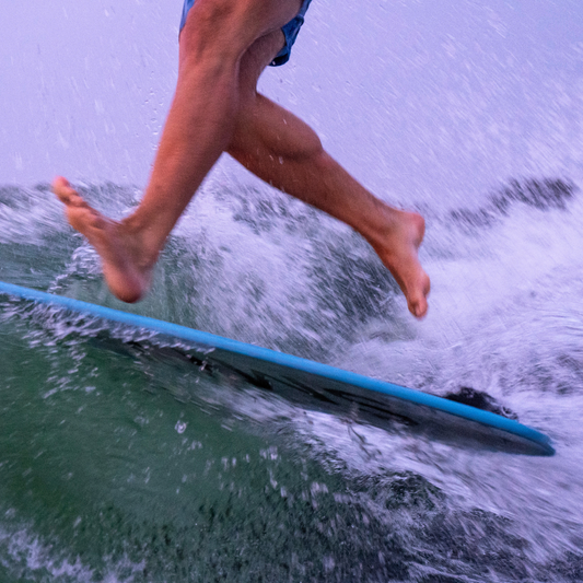 Close-up of a wakesurfer’s feet performing a quick movement on a blue wakesurf board, skimming across the wave to show balance and agility on the water.